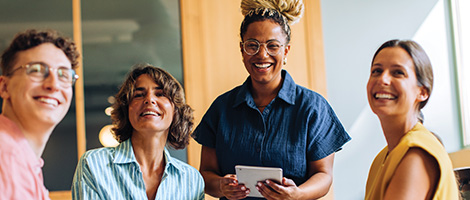 A diverse group of middle-aged and young adult professionals smile and look happy, representing the supportive and helpful team clients can connect with at HM Insurance Group's home office for various inquiries.