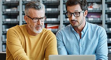 Two middle-aged professionals are intently focused on a laptop screen, representing the operational excellence and deep industry understanding that gives HM Insurance Group clients confidence in their protection.