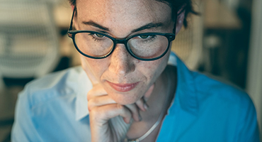 A middle-aged professional wears glasses and looks thoughtfully at a laptop screen, representing the careful consideration and individualized solutions that HM Insurance Group's underwriters provide to address client risk tolerance.