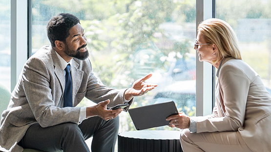 Two middle-aged professionals are engaged in a serious conversation while looking at a tablet, representing HM Insurance Group's understanding of the rising stakes in healthcare and their commitment to financial stability for clients.