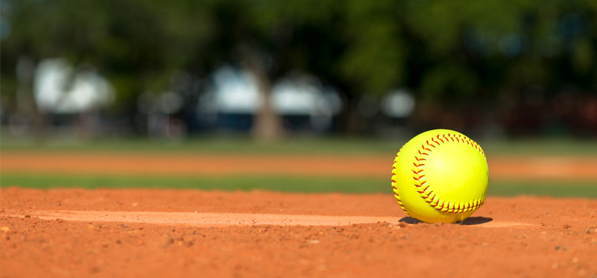 A softball placed on the ground near the softball field's pitching mound.