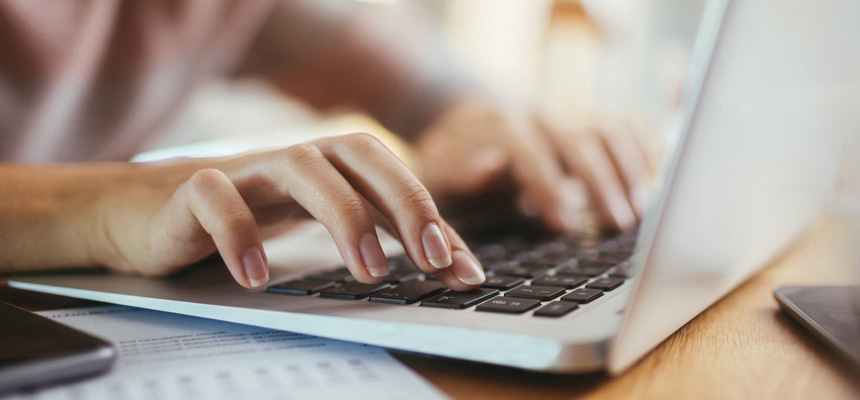 A seated person's hands typing on a laptop while using HM eServices.