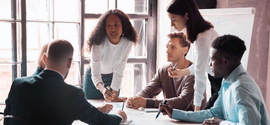 A team of business people are gathered around a table, talking and working together.