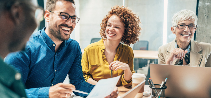 A group of four people, two male and two female, are sitting at a table talking and laughing while reviewing HM materials.