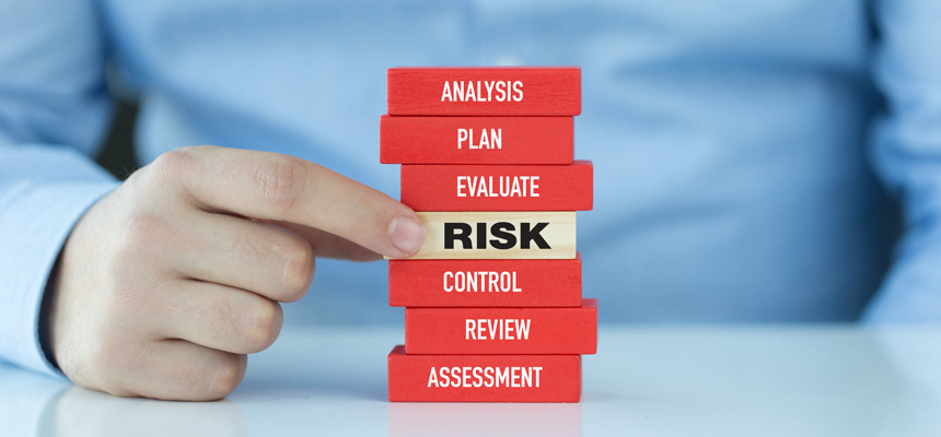 A stack of seven stacked blocks, including six red with labels Analysis, Plan, Evaluate, Control, Review and Assessment, has a man pointing to the center wood-colored block labeled Risk.