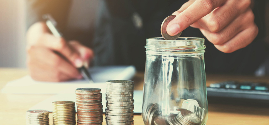 A person counting change has created four stacks of coins and is placing one coin in a jar while taking notes.