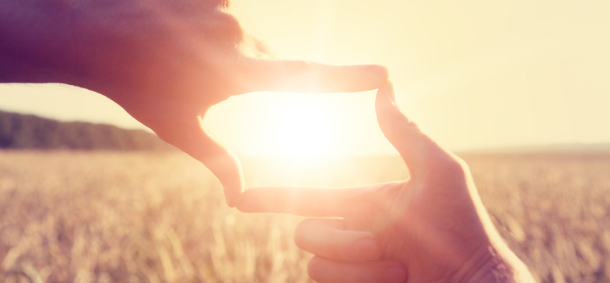 Two hands framing a sunset in a field of wheat.