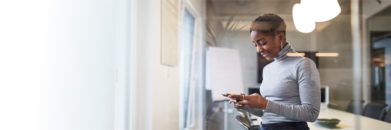 A female insurance broker is standing in a conference room while looking at HM materials on the mobile device she's holding.