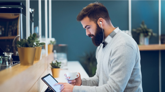 A seated man wearing earbuds reads an HM Industry Insights blog post on a mobile debice while holding a coffee cup.