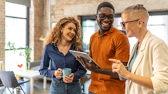 Three young adult professionals smile while looking at a tablet together, representing the engaging and insightful content shared by HM Insurance Group's leaders in their Industry Insights Blog.