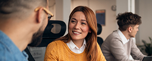 A smiling middle-aged professional looks at another professional while seated at a desk, representing the trusted relationships and integrity that define how HM Insurance Group works with clients.