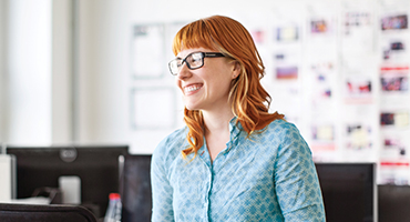 A smiling young adult in glasses looks happily to the side in a bright office, showing the satisfaction and trust clients have in HM Insurance Group's 40 years of direct writing and tailored solutions.