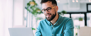 A young adult professional smiles while looking at a laptop, representing how HM Insurance Group's industry insights and expert thoughts are easily accessible and engaging for clients.