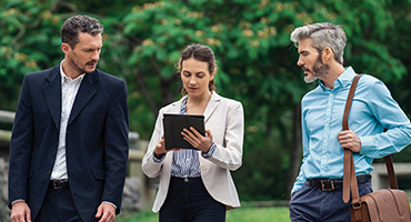 A middle-aged professional and two young adults walk outside while looking at a tablet, representing the collaborative strength and transparent communication that HM Insurance Group uses to deliver financial protection.