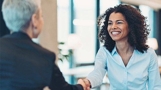 A female insurance broker wearing professional clothes shake shands with a female client and smiles..