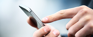 A person's hands are shown up close, tapping on a smartphone, representing the easy and direct way to connect with HM Insurance Group to discuss reinsurance and excess insurance solutions.