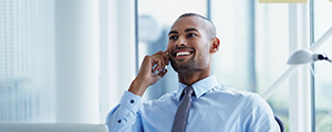 A male insurance agent wearing professional clothes is seated wtih a laptop while talking on a mobile device.