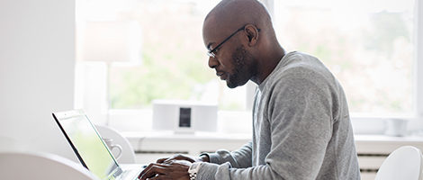 A man is seated near a window and working on a laptop.