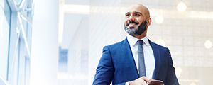 A male insurance broker wearing professional clothes looks away while holding a mobile device.